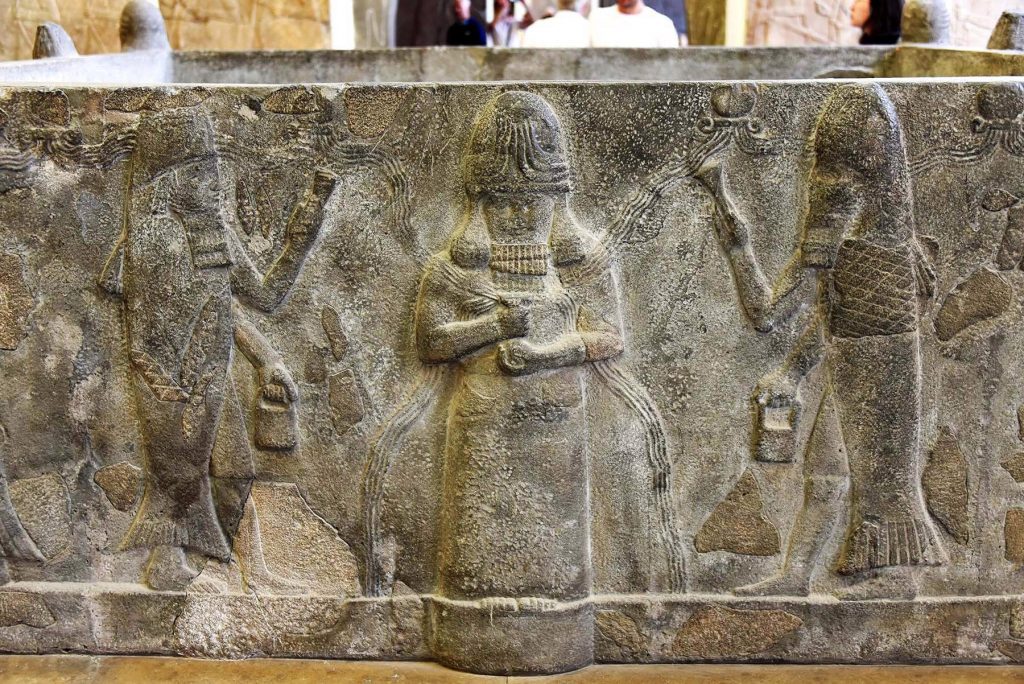 Enki (Ea) flanked by a pair of fish-apkallus. Carving on a basalt water basin from Assur, Iraq, 7th century BCE.